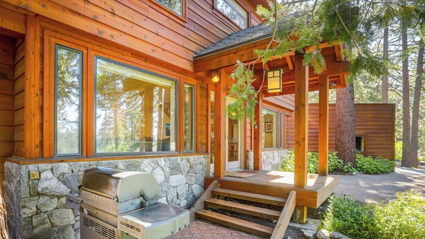 A wooden cabin with large windows, a stone wall, and a grill outside. - Spacious Tahoe City Retreat < 2 Mi to Lake Tahoe! (Tahoe City)