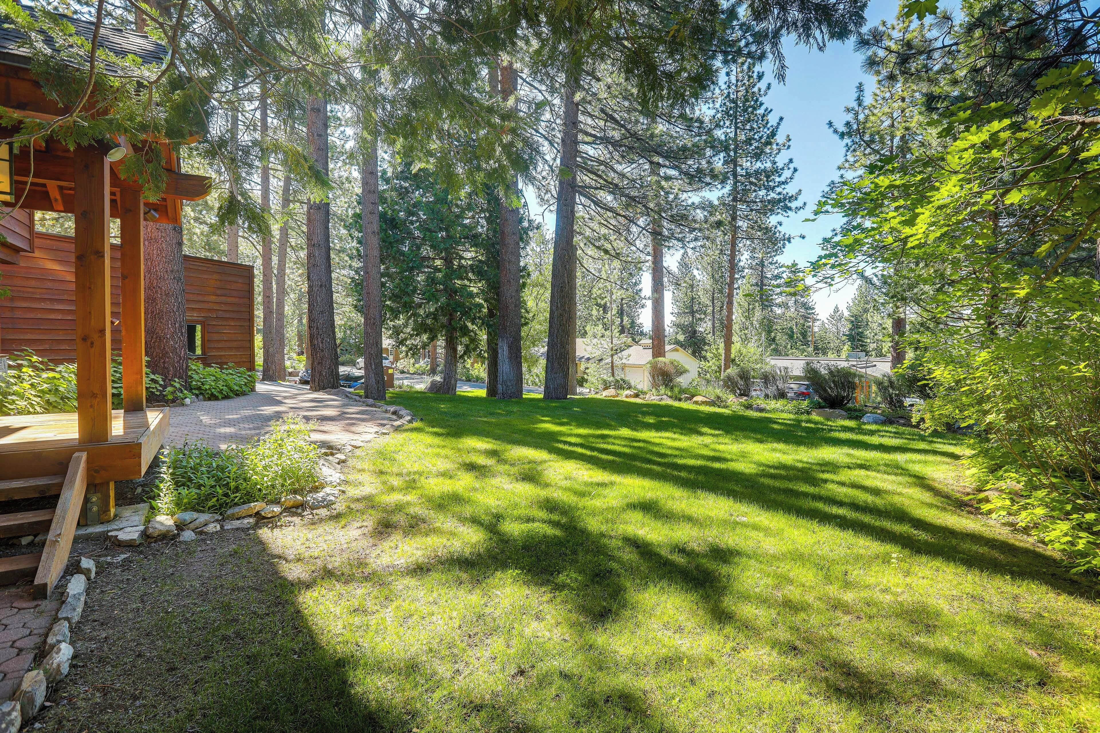 A wooden deck with a stone pathway leading to a grassy area surrounded by tall trees.