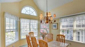 A dining room with a wooden table and chairs, large windows with blinds, a chandelier, and a vase with flowers. - Ocean City Home 1 Block to Beach & Boardwalk! (Ocean City)