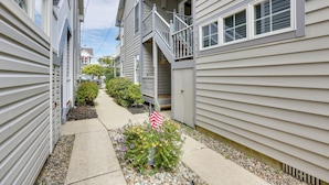 A narrow residential street with houses on both sides, a small garden with flowers and an American flag, and a clear sky. - Ocean City Home 1 Block to Beach & Boardwalk! (Ocean City)