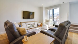 Een moderne woonkamer met leren banken, een houten salontafel en een flatscreen televisie aan de muur.
