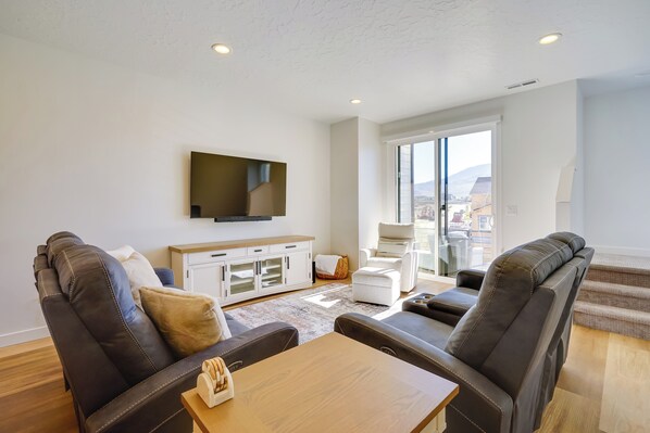 A modern living room with leather sofas, a wooden coffee table, and a flat-screen TV mounted on the wall. - Mountain Green Luxury Retreat By Snowbasin Resort! (Mountain Green)