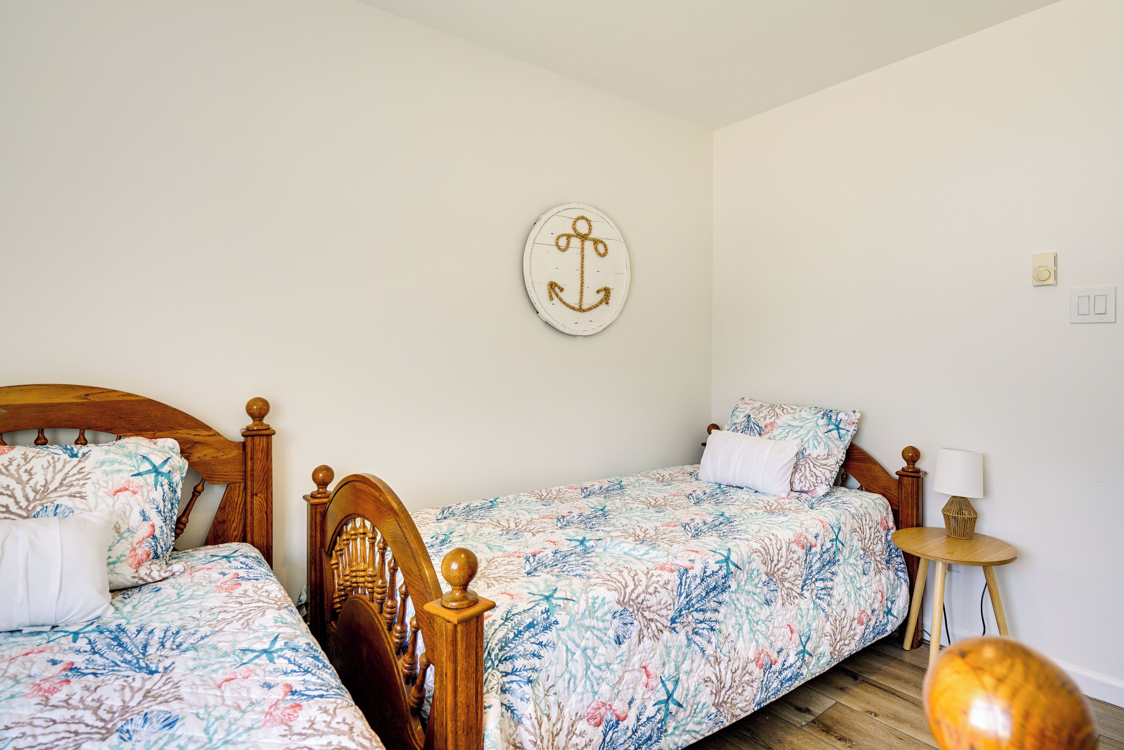 A bedroom with two wooden beds, floral bedding, a round wall decoration, a bedside table with a lamp, and a small round table.