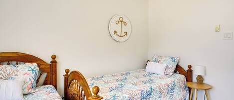 A bedroom with two wooden beds, floral bedding, a round wall decoration, a bedside table with a lamp, and a small round table.
