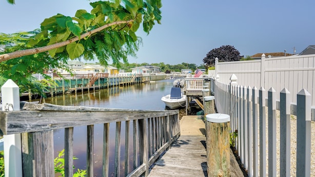 A narrow waterway with a wooden walkway, boats docked, and a white fence on one side. - Charming Beach Haven West Home: 1 Mi to Beach! (Manahawkin)