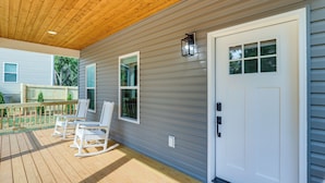A covered porch with wooden flooring and white rocking chairs, a white door with a window, and a small wall-mounted light fixture. - Getaway w/ Fire Pit: 3 Mi to River Arts District! (Asheville)