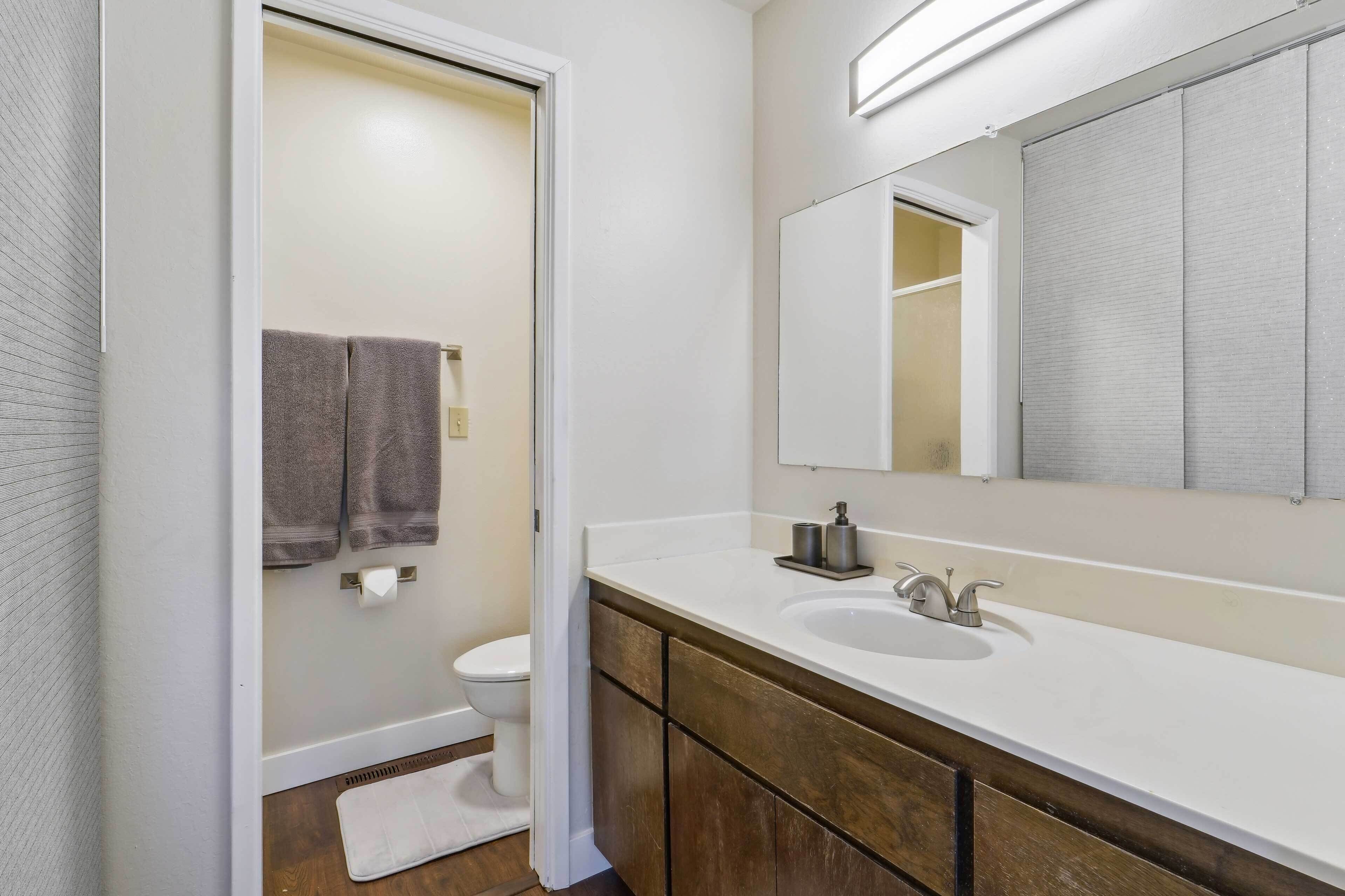 Un baño con lavamanos blanco, tocador de madera y un espejo grande.
