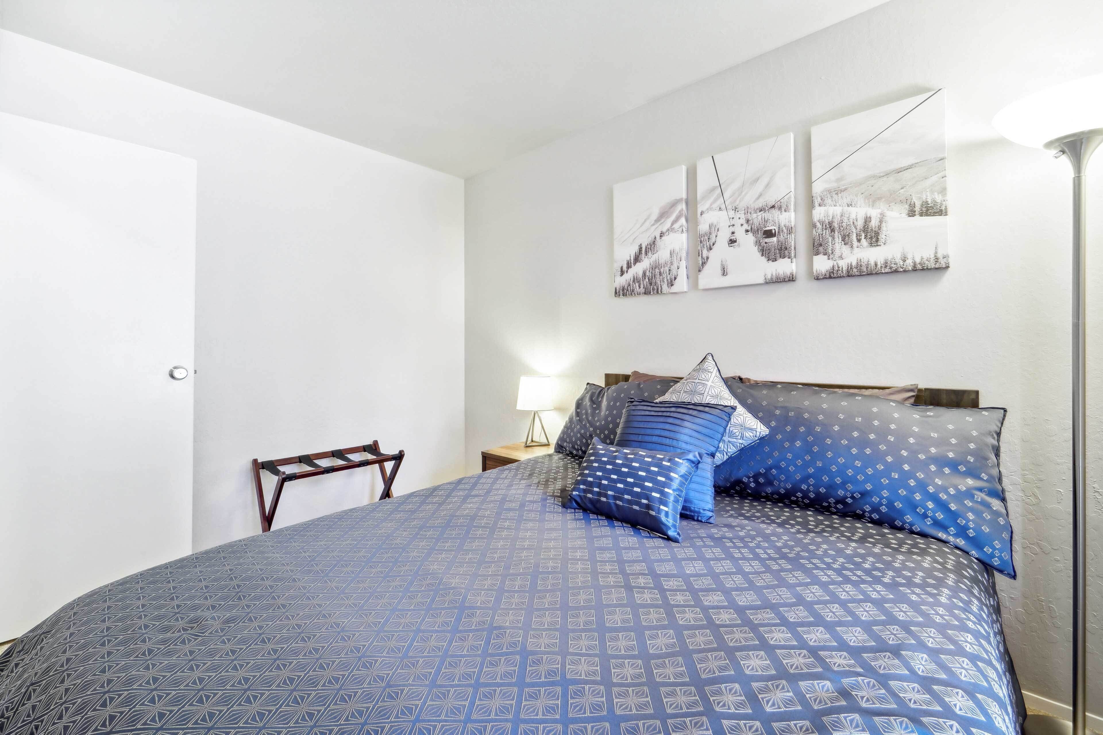 A bedroom with a large bed, a nightstand, a lamp, and three wall-mounted pictures.
