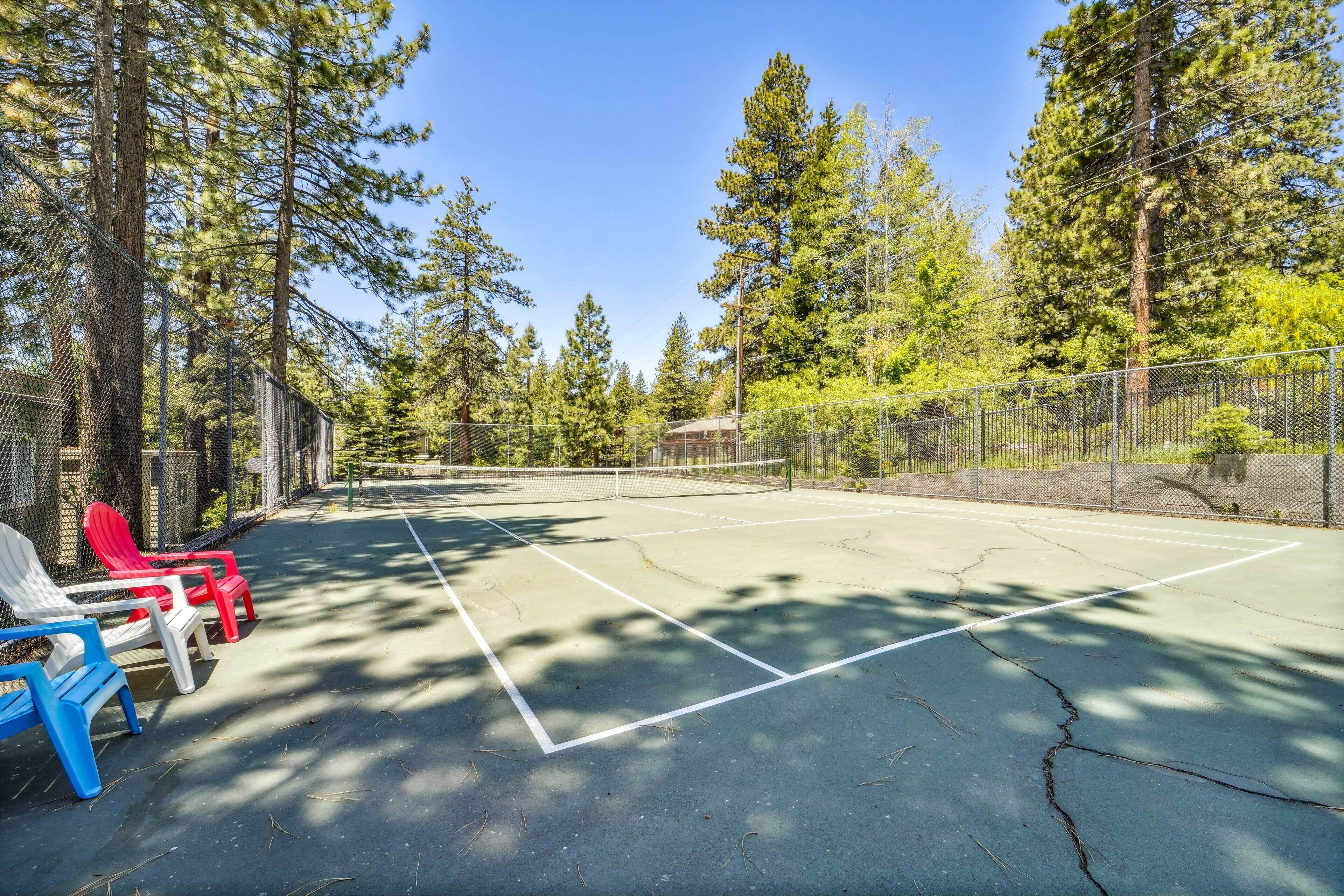 A tennis court with a net, surrounded by tall trees and a fence.