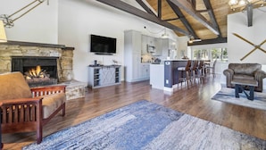 A spacious living area with a stone fireplace, wooden beams, a kitchen with grey cabinets, and a bar area. - 10 Mi to Palisades Tahoe! Condo w/ Game Room (Tahoe City)
