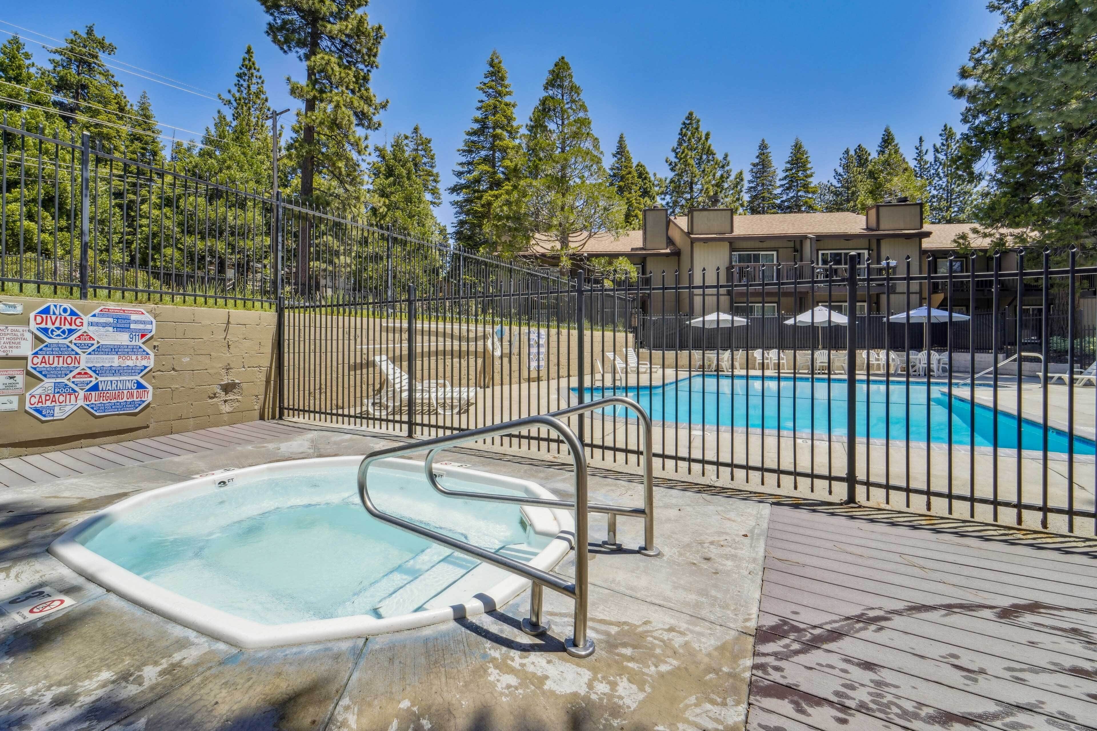 A swimming pool area with a hot tub, surrounded by a fence, and a building in the background.