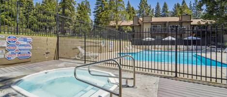 A swimming pool area with a hot tub, surrounded by a fence, and a building in the background.