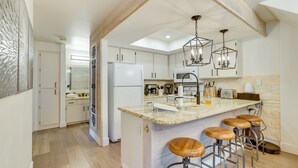 A modern kitchen with white cabinets, a central island with stools, a refrigerator, a microwave, and hanging pendant lights. - Brian Head Rental w/ Community Hot Tub & Sauna! (Brian Head)
