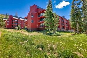 A red multi-story building with balconies, surrounded by green grass and trees. - Brian Head Rental w/ Community Hot Tub & Sauna! (Brian Head)