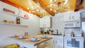Une cuisine avec des meubles blancs, un plafond en bois et un îlot central doté de tabourets.