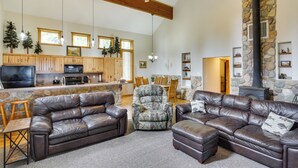 A spacious living area with leather sofas, a stone fireplace, and a kitchen with wooden cabinets and a stone accent wall. - Spacious Beaver Getaway Near Eagle Point Resort! (Beaver)