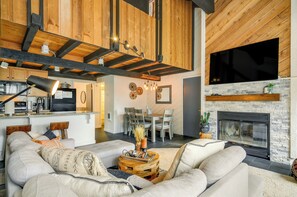 Una sala moderna con sofá, mesa de centro y chimenea. Hay una zona de comedor con una mesa y sillas, y una cocina al fondo.