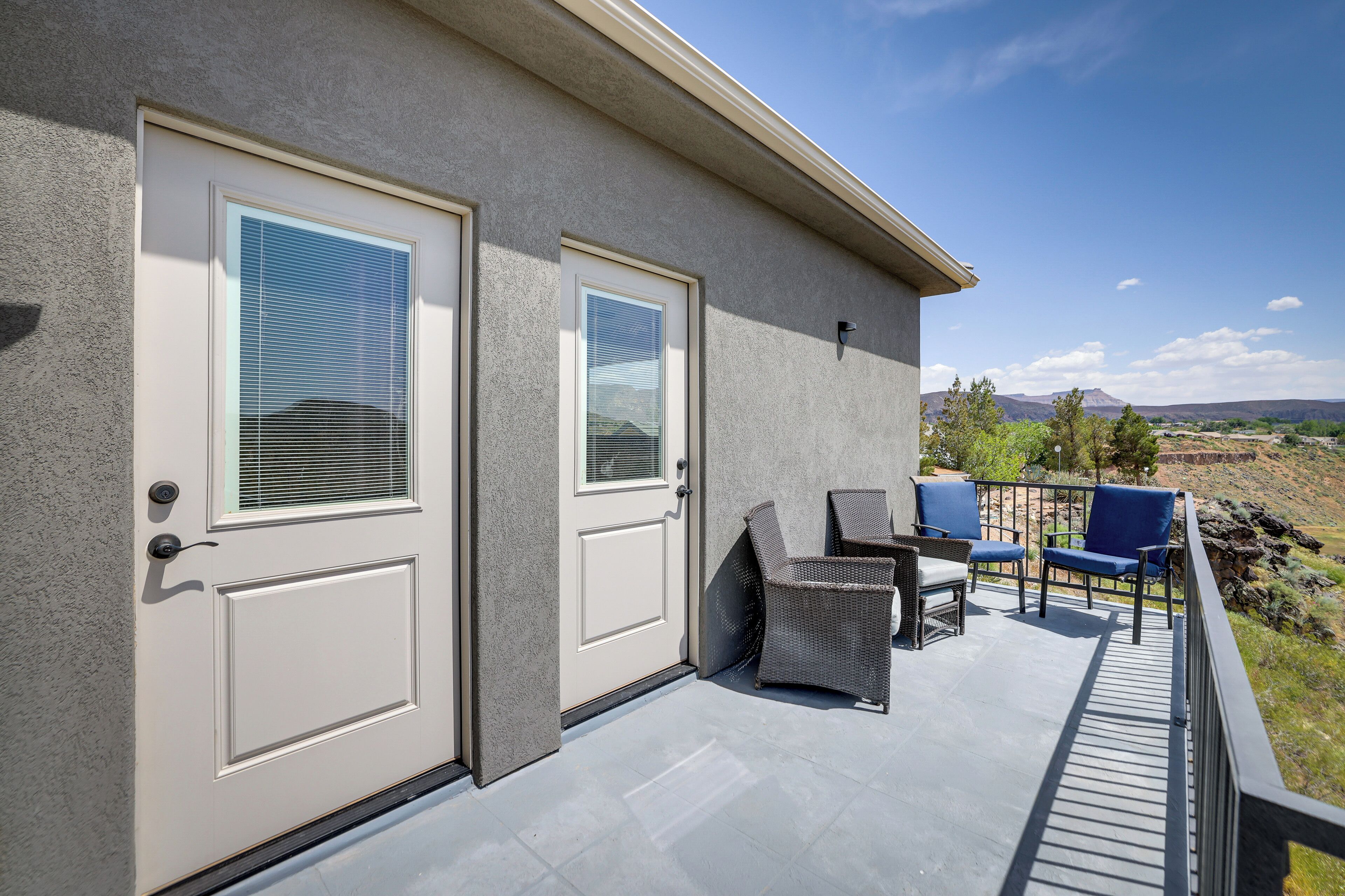 A building with two doors, a balcony with wicker furniture, and a view of the landscape.