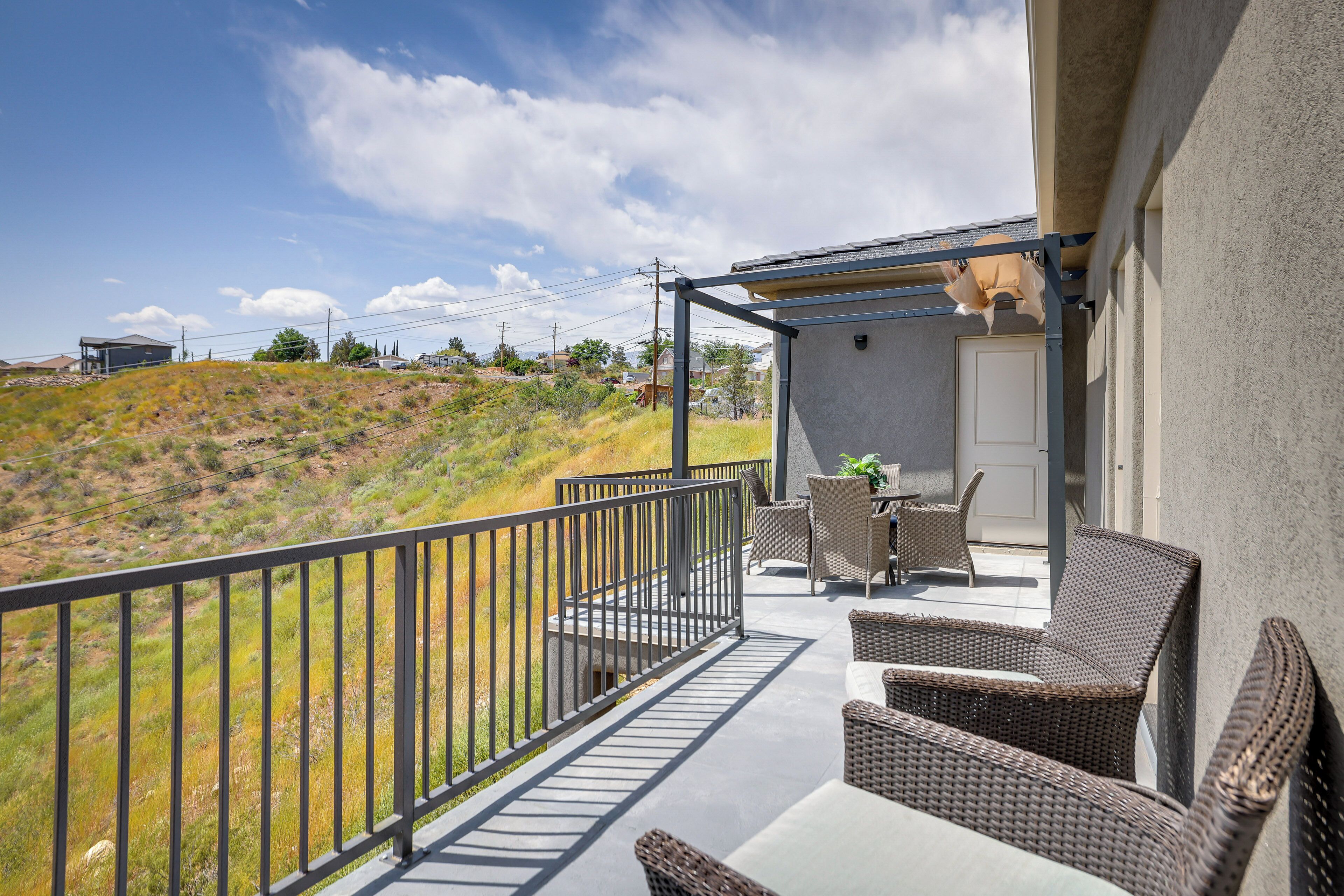 A balcony with wicker furniture, a door, and a view of a hilly landscape.