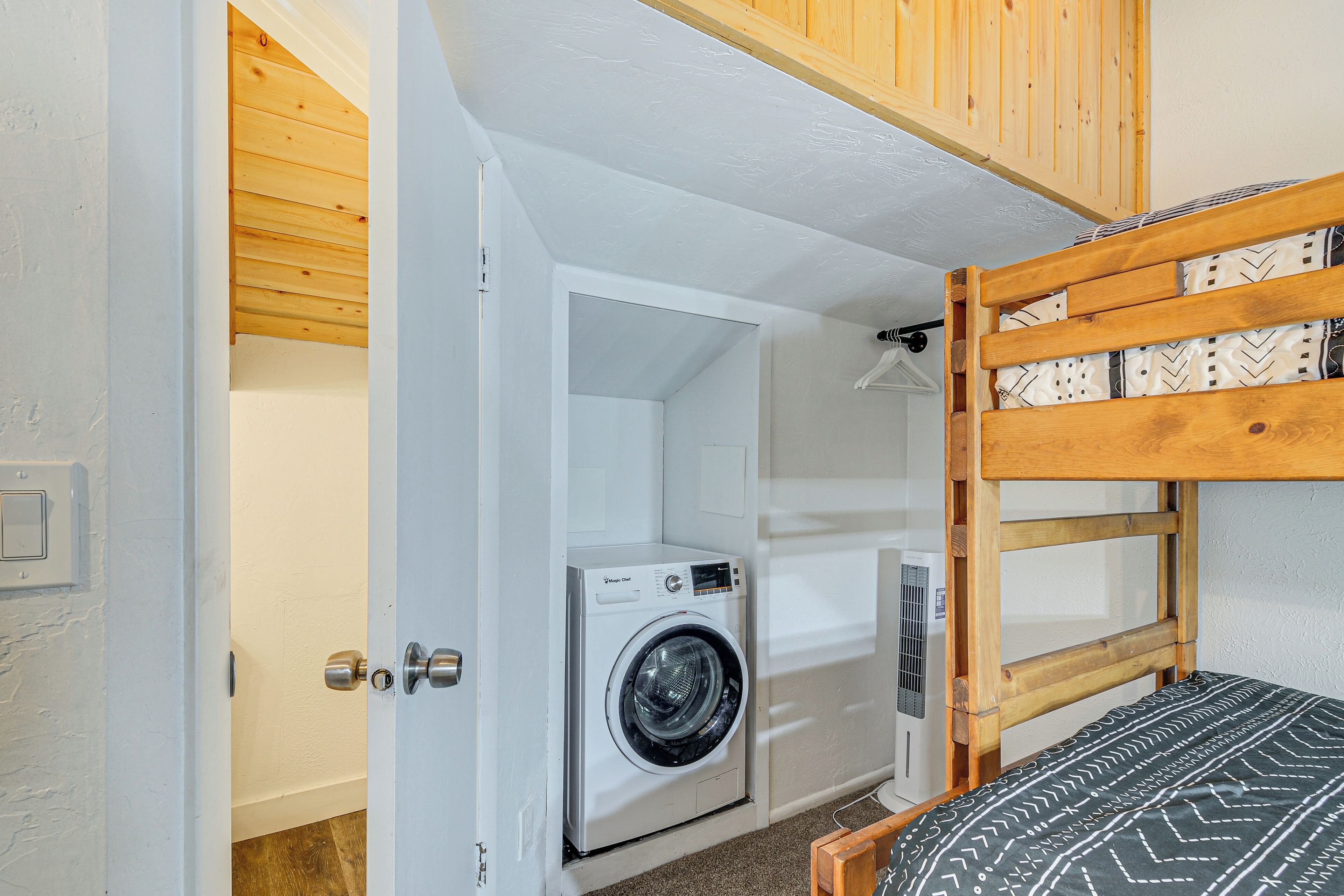 Een kleine kamer met een wasmachine, een stapelbed en een deur naar een andere kamer.