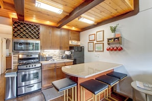 A modern kitchen with stainless steel appliances, wooden cabinetry, and a bar area with stools.