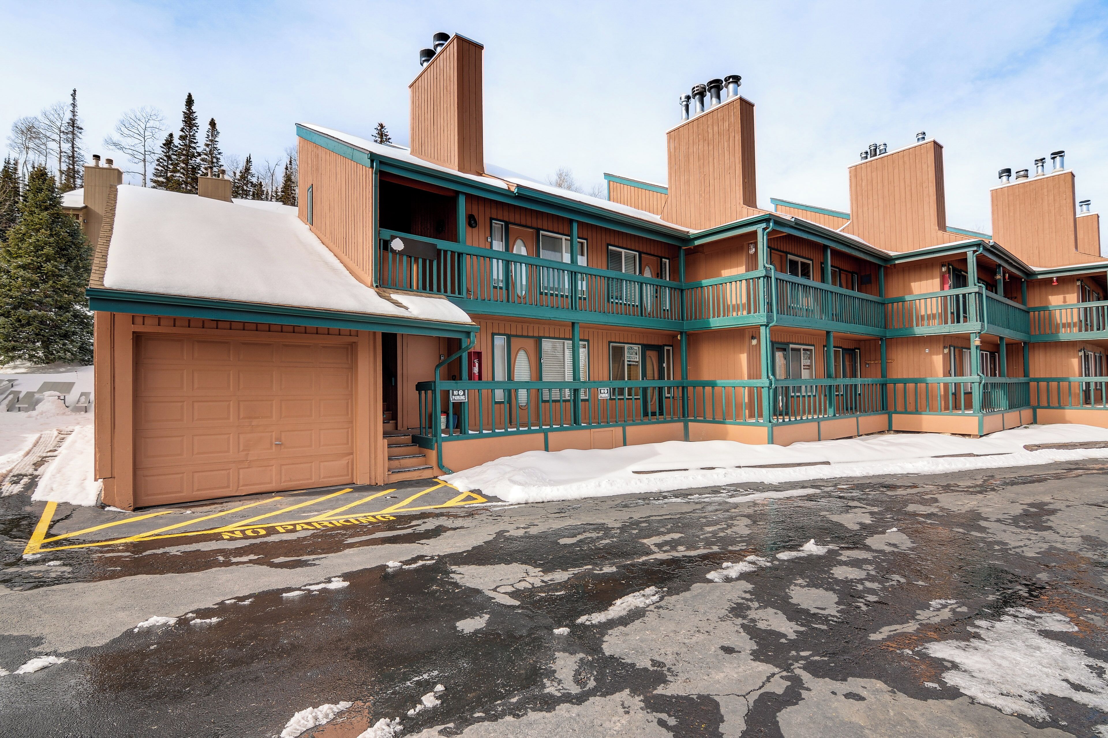 Un edificio de varios pisos con garaje, balcones y el suelo cubierto de nieve.