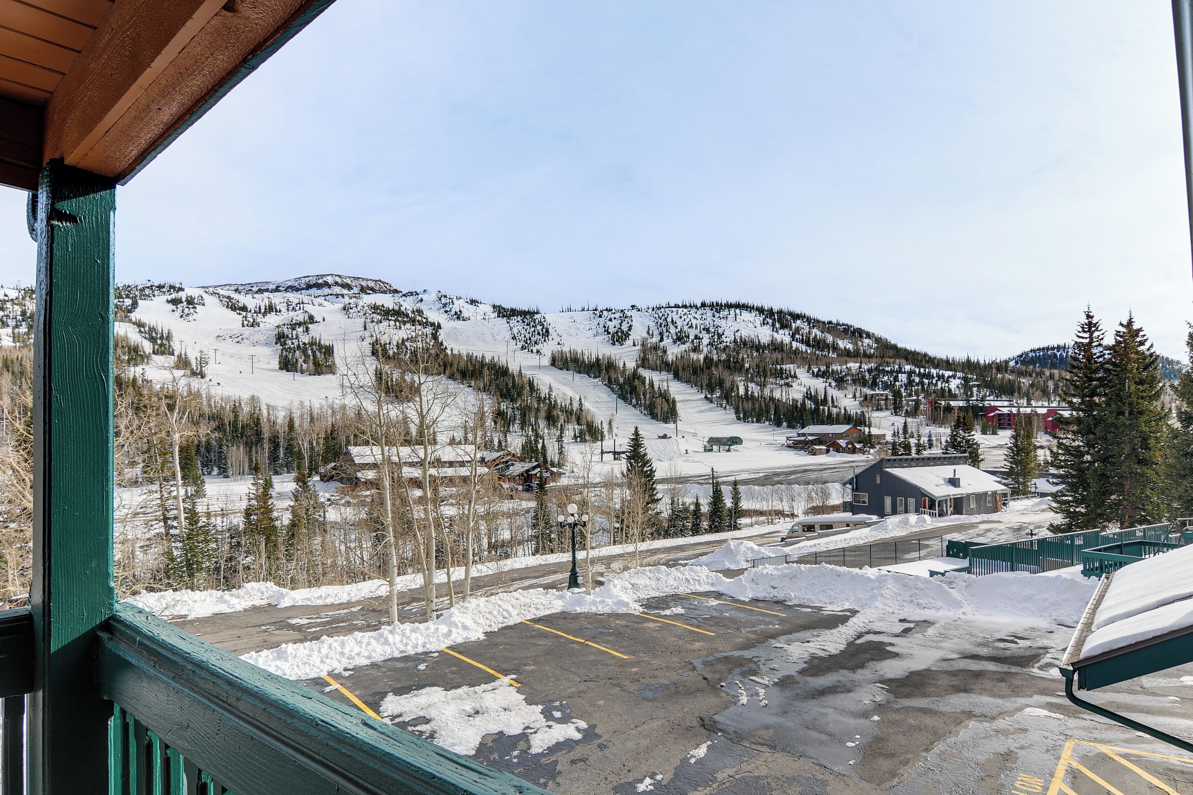 Vista desde el interior de un edificio hacia un estacionamiento cubierto de nieve y una estación de esquí con edificios y árboles.