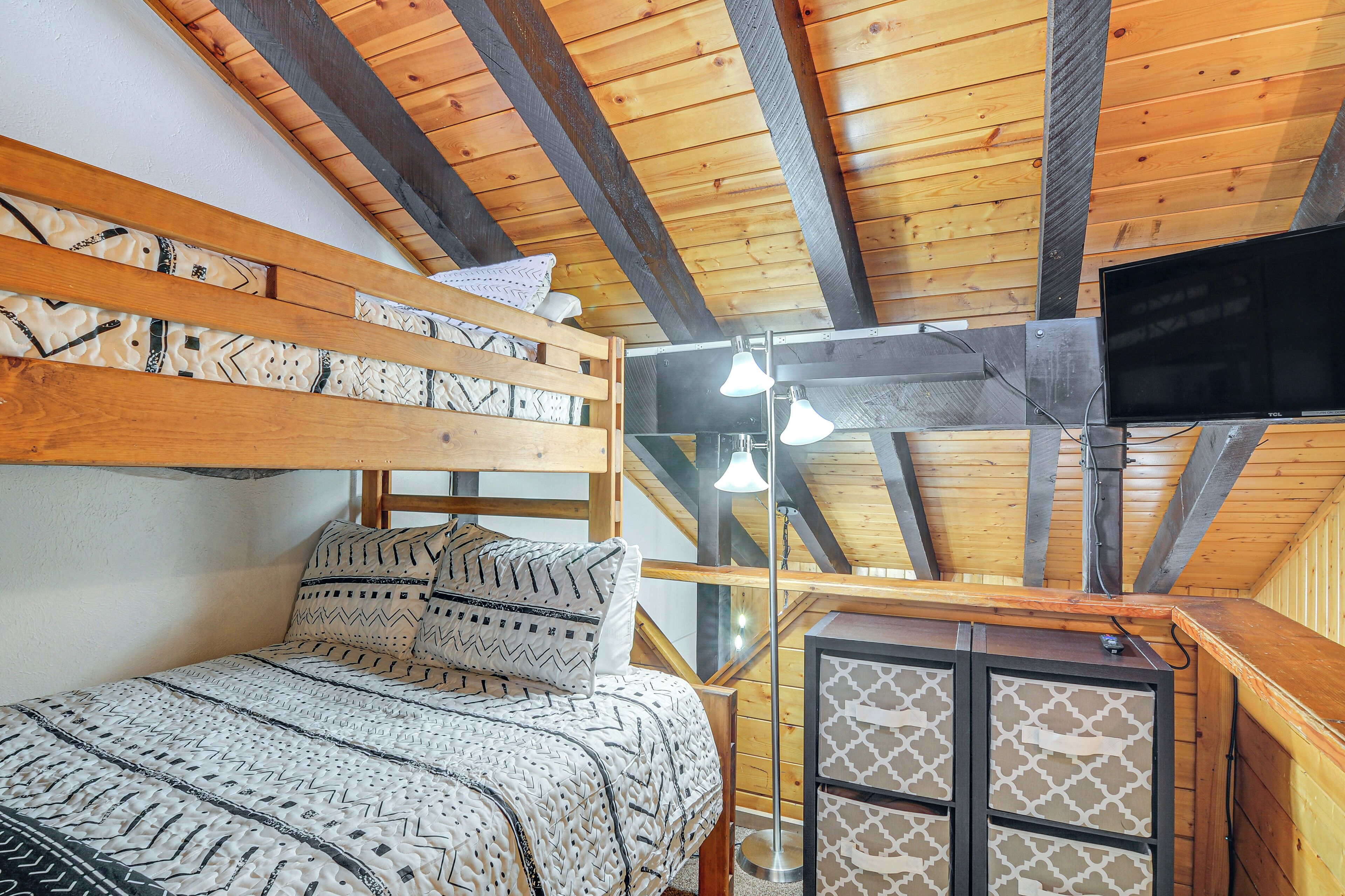 A loft-style bedroom with a bunk bed, a desk with a flat-screen TV, and a ceiling fan.
