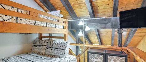A loft-style bedroom with a bunk bed, a desk with a flat-screen TV, and a ceiling fan.