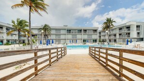 A wooden boardwalk leading to a pool area with a building in the background. - Ocean-view Key Colony Beach Condo w/ Pool Access! (Key Colony Beach)