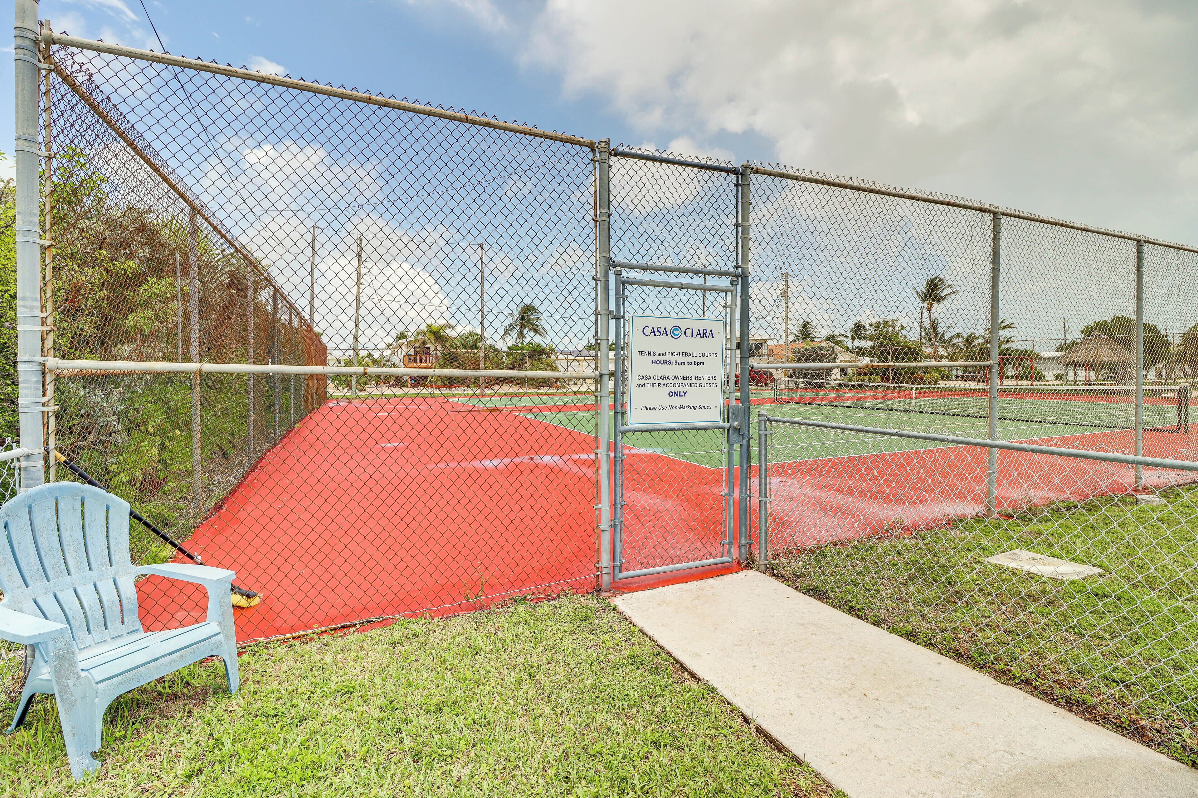 A fenced tennis court with a sign for Casa Clara, a bench, and a clear sky.