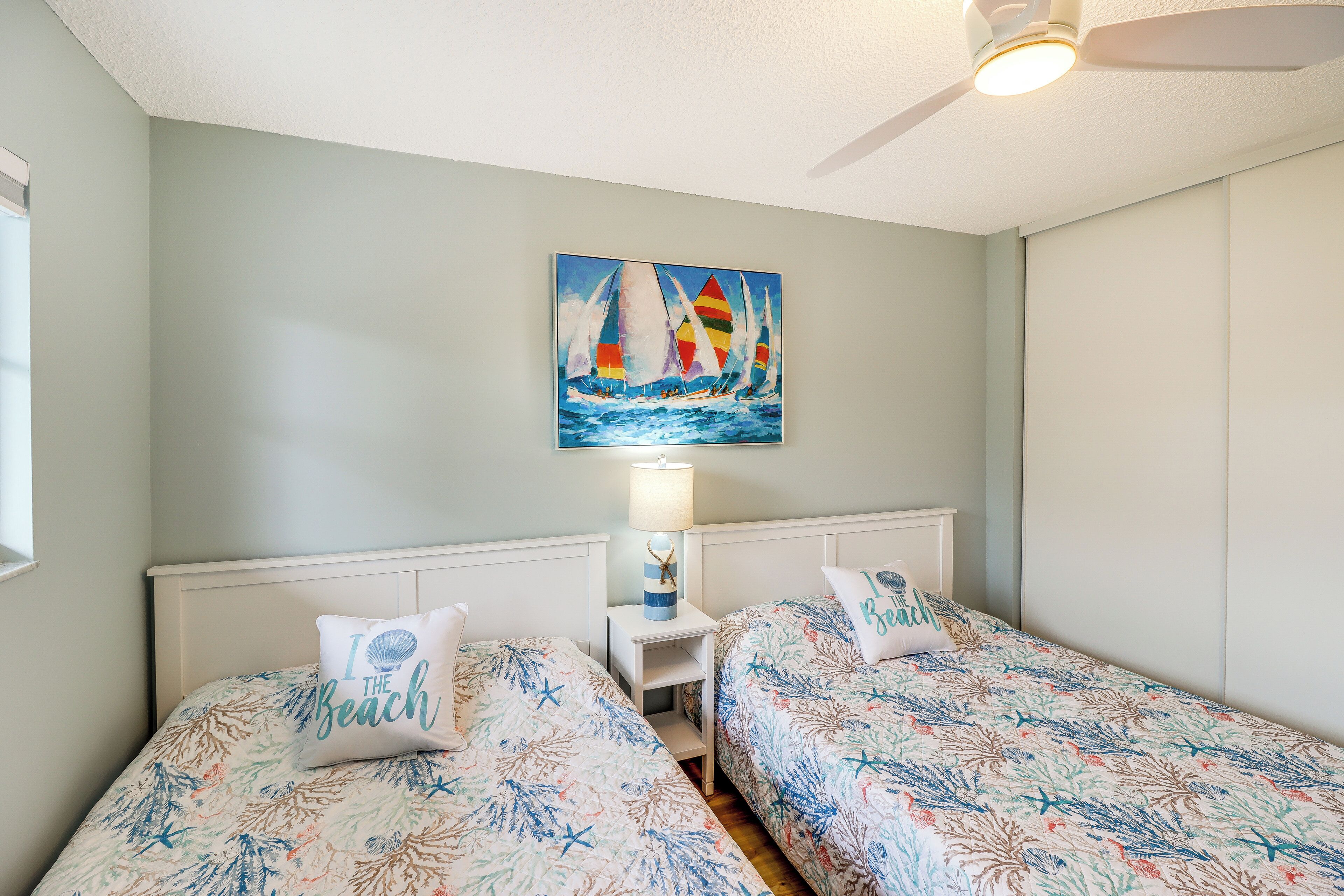 Ein Schlafzimmer mit zwei Betten, einem Deckenventilator und einem Bild von Segelbooten an der Wand.
