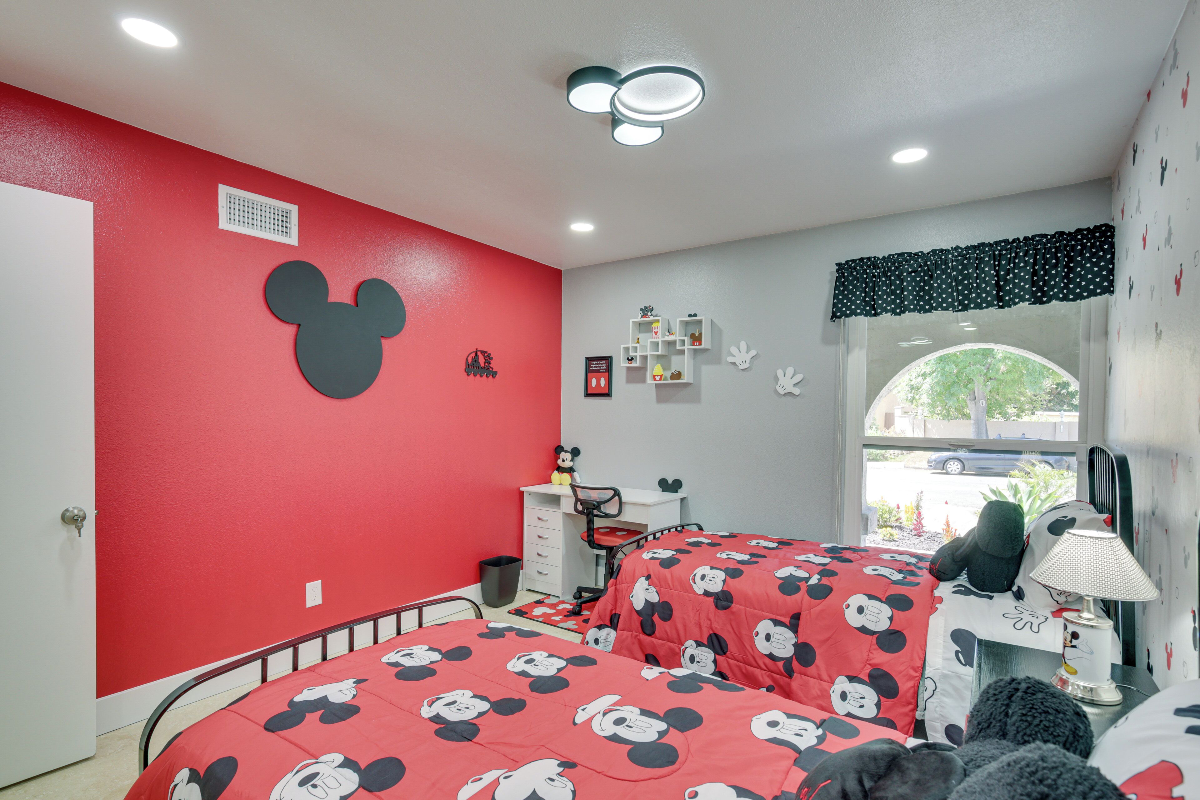 A room with two beds, a desk, and a window with a view of the street.