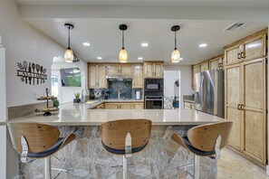A modern kitchen with a large island, wooden cabinets, stainless steel appliances, and pendant lighting.