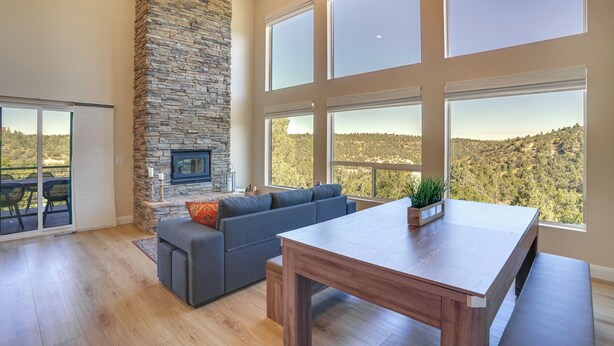 Un salón amplio con chimenea de piedra, ventanas grandes, un sofá gris y una mesa de comedor de madera.