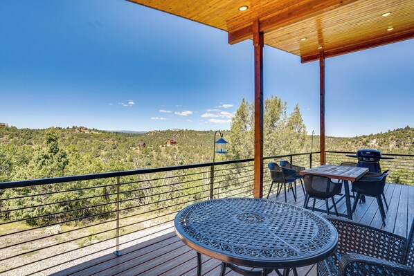 A wooden deck with a table and chairs, overlooking a hilly landscape.