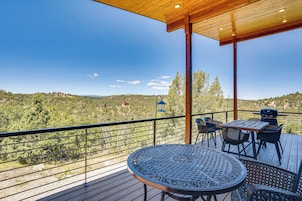 A wooden deck with a table and chairs, overlooking a hilly landscape.