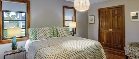 A bedroom with a large bed, two bedside lamps, a wooden door, and a window with a view.
