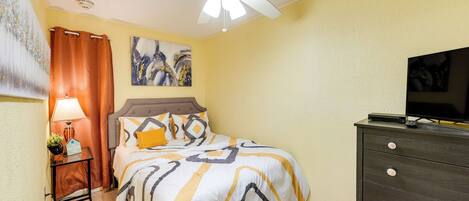 A bedroom with a bed, a nightstand, a dresser, a ceiling fan, and a painting on the wall.