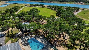 A residential property with a swimming pool, surrounded by trees and a view of a lake. - Lago Vista Home w/ Game Room & Outdoor Tub! (Leander)