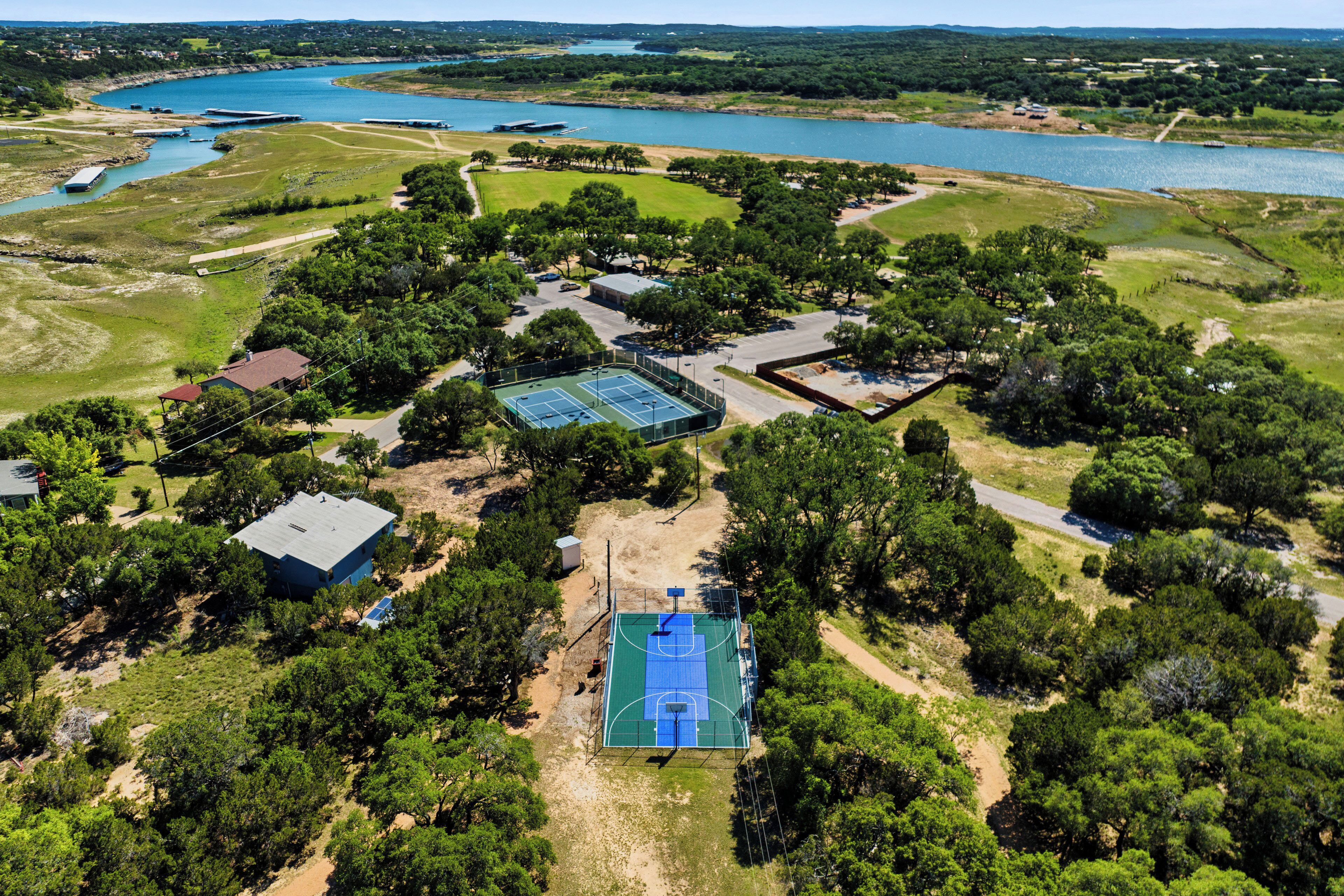 Luchtbeeld van een bezit met een tennisbaan, meerdere gebouwen en een groot waterlichaam op de achtergrond.