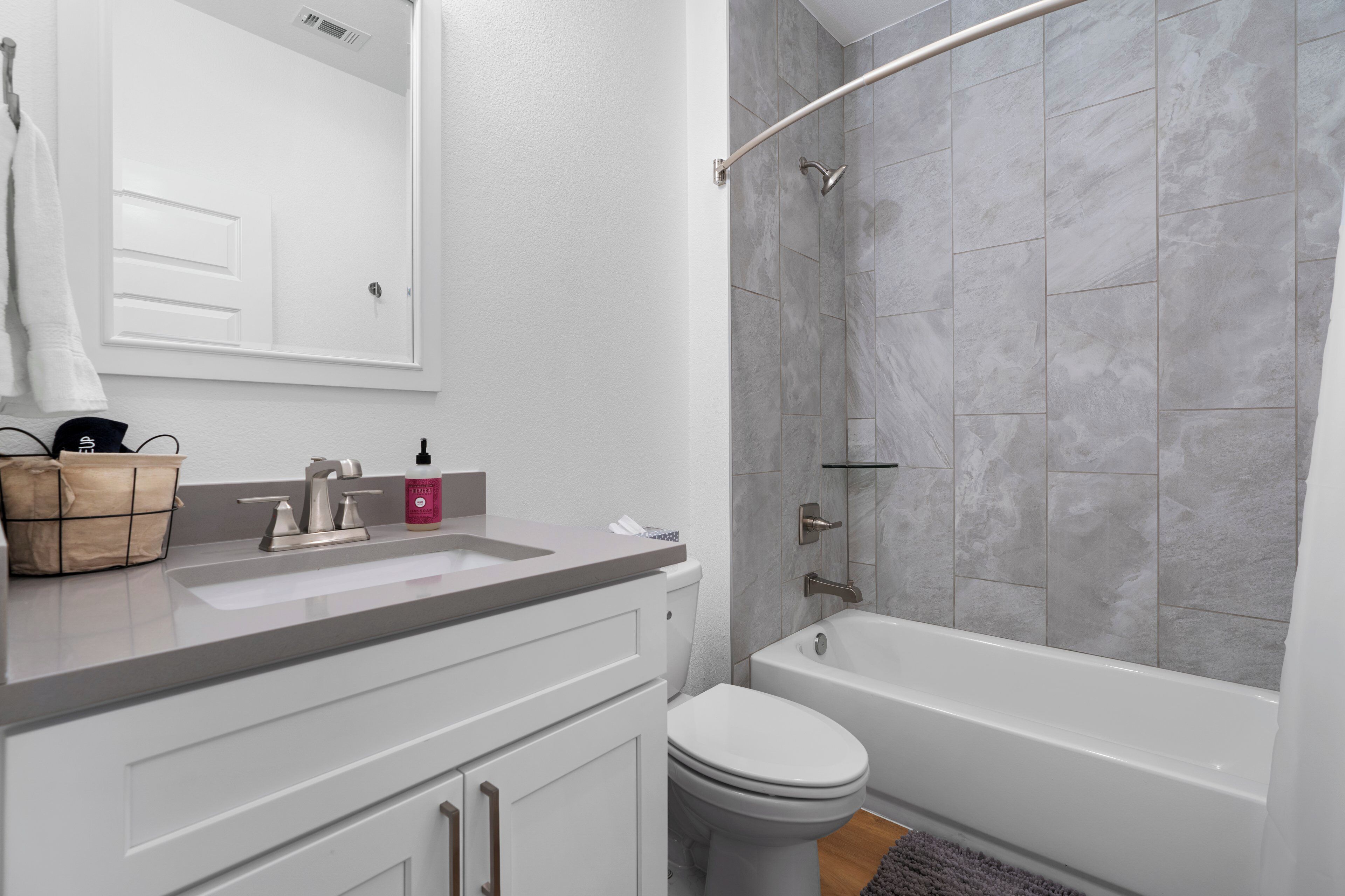 Une salle de bain moderne avec un lavabo, des toilettes et une baignoire, tous de couleur blanche. Une serviette est accrochée au mur et un petit panier en bois est posé sur le comptoir.