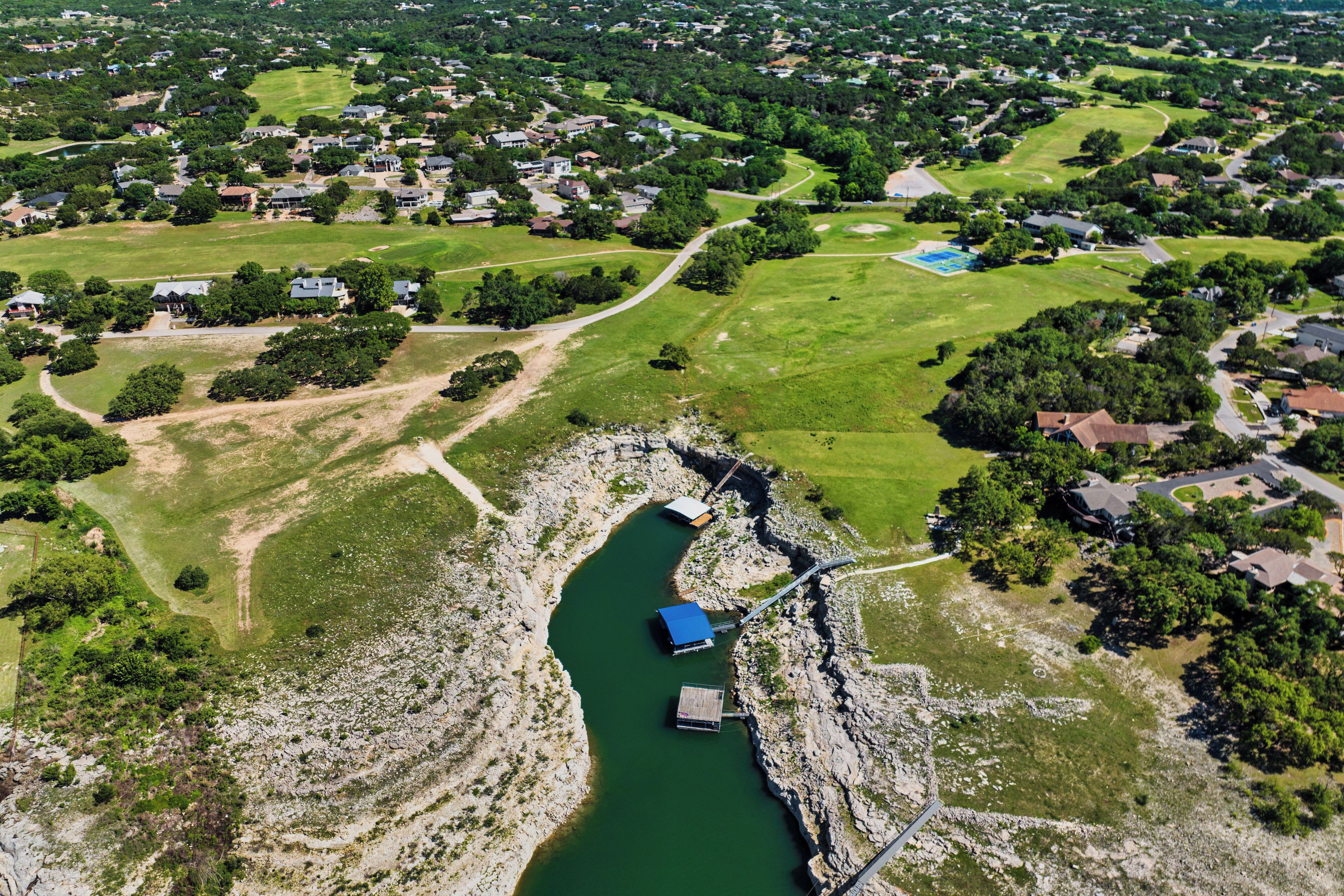 An aerial view of a residential area with houses, green spaces, and a river with docks.