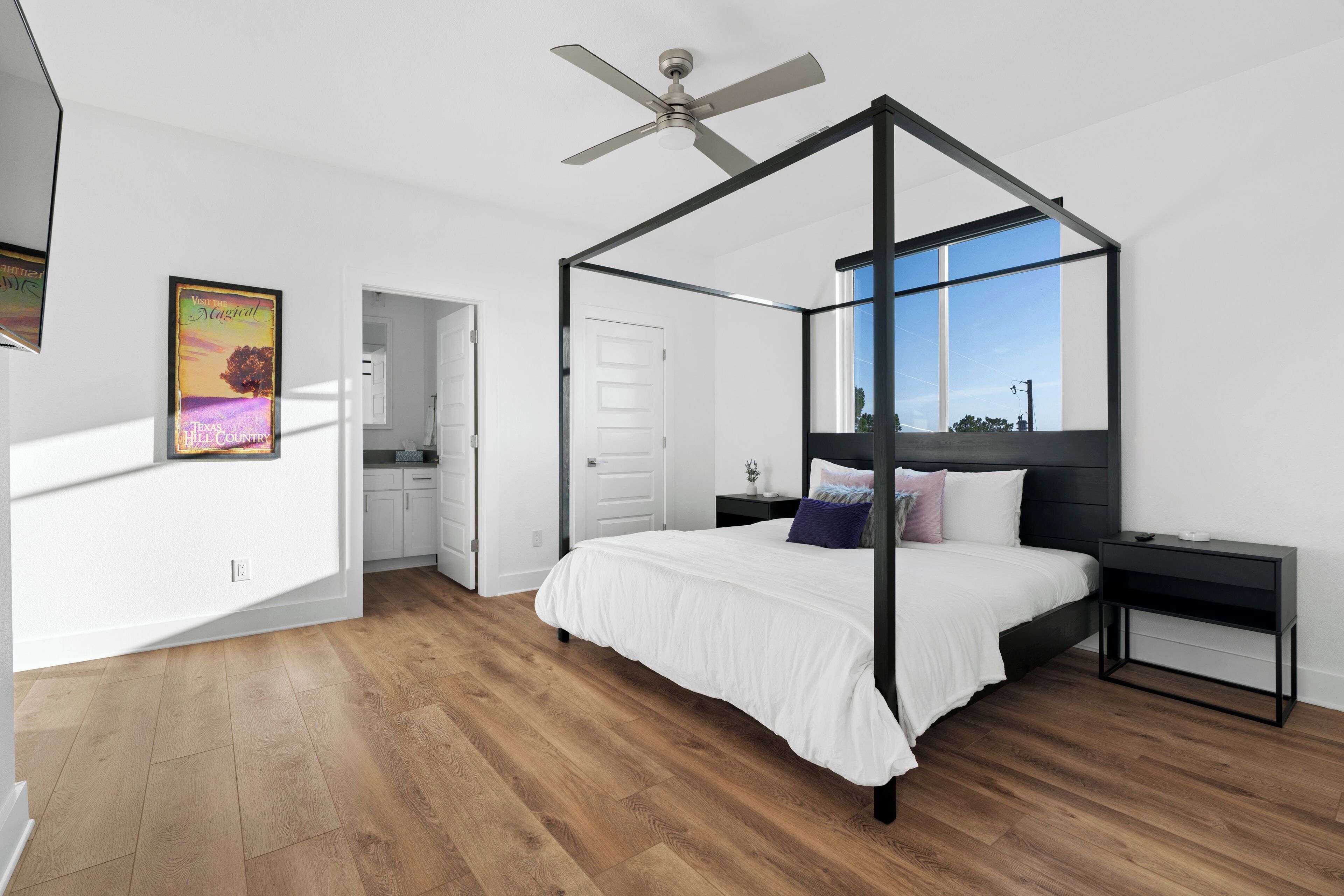 Une chambre moderne avec un lit à baldaquin, un ventilateur de plafond et une grande fenêtre donnant sur l’extérieur.