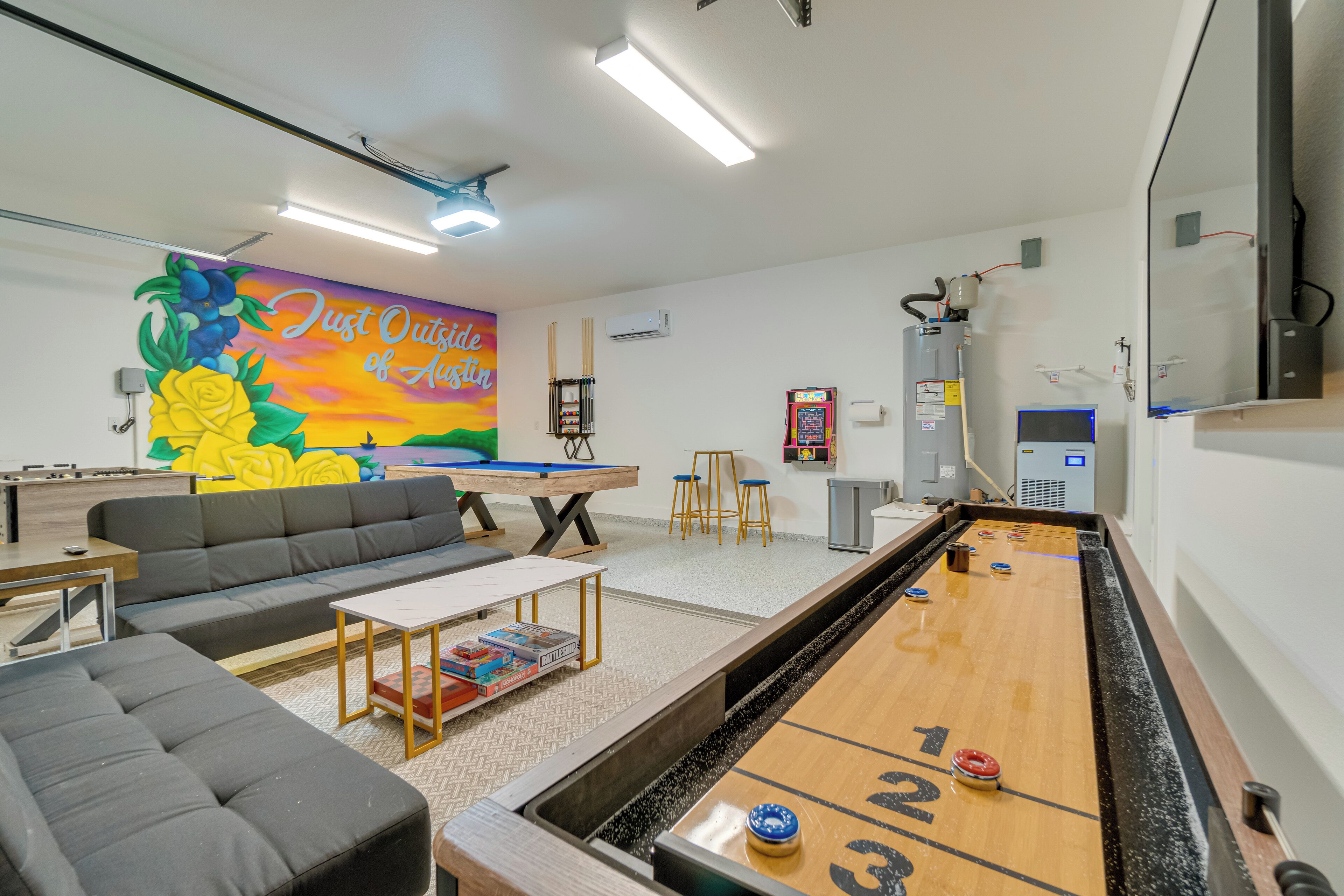 A billiards room with a shuffleboard table, a sofa, and a mural on the wall.