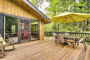 A wooden deck with outdoor furniture, a glass door leading to an interior dining area, and a yellow umbrella. - Jamaica Vacation Home w/ Deck: 8 Mi to Skiing! (Jamaica)