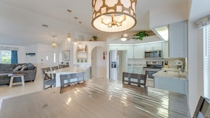 Ampla sala de estar com uma grande mesa de jantar de madeira, cozinha equipada com eletrodomésticos modernos e um ventilador de teto.