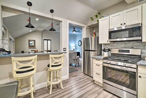 Una cocina moderna con armarios blancos, electrodomésticos de acero inoxidable y dos taburetes de bar.