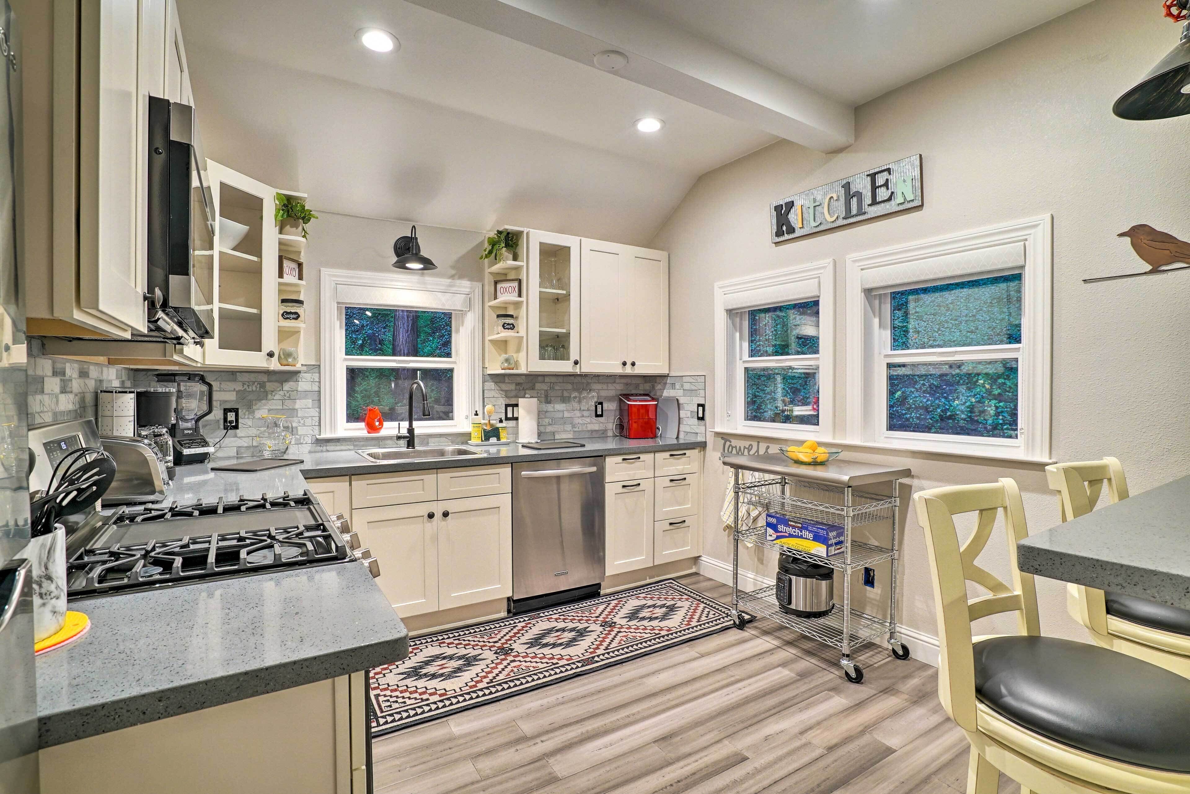 A modern kitchen with white cabinets, a gas stove, a dishwasher, and a window with a view.
