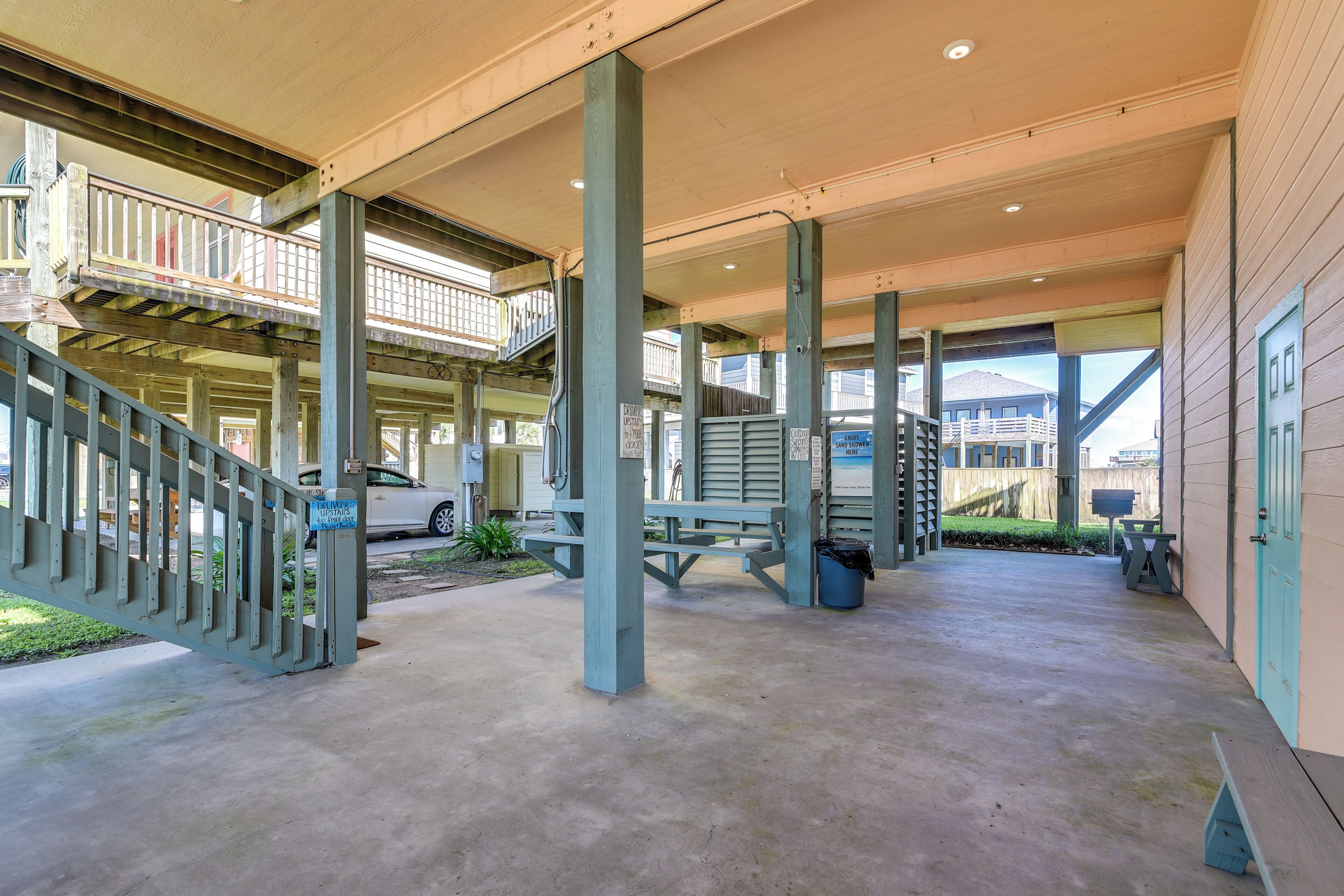 A covered outdoor area with concrete flooring, wooden benches, and a staircase leading to an upper level.